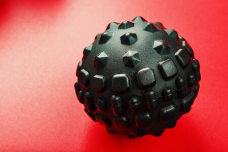 Black lumpy foam body massage ball on red background. For the mechanical and reflex effects on tissues and organs.の写真素材