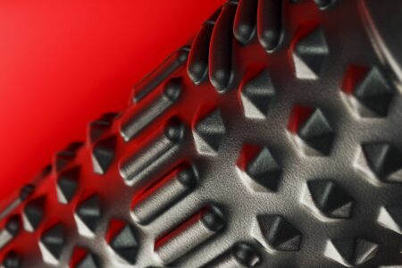 Black lumpy foam massage roller on red background. For the mechanical and reflex effects on tissues and organs. Close-up, texture, element in macroの写真素材