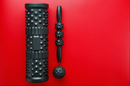 Set of Black lumpy foam massage roller, body roller, rubber ball on red background. For the mechanical and reflex effects on tissues and organs.の写真素材