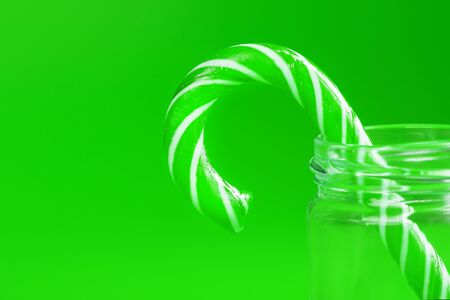 One Lollipop Candy cane in a glass jar on a green background. The concept of minimalism, free space for text.の写真素材