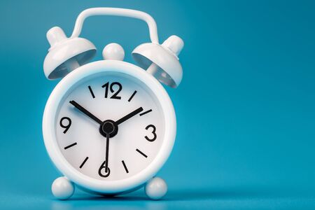 White retro alarm clock on blue background. Concept of time with free space for text. Minimal style, close-up.の写真素材