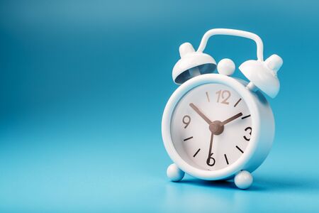 Alarm clock white on a blue background 13-50. Concept of time with free space for text. Minimal styleの写真素材