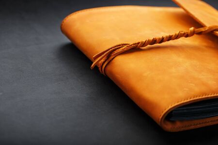 The leather cover of the album is made of brown handmade genuine leather on a black background. Elements of a leather product close-up. Craft, low contrastの写真素材