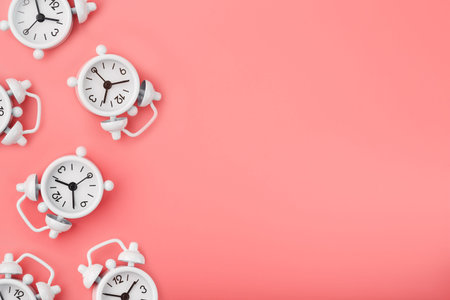 A pattern of many white classic alarm clocks in the form of a pattern on a pink background. Top view...