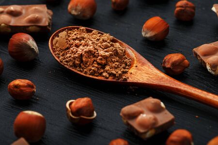 Chocolate with hazelnuts and a wooden spoon with cocoa on a dark background, surrounded by nuts in the shell and peeled. Still-life of Confectionery products. Top view, close-upの写真素材