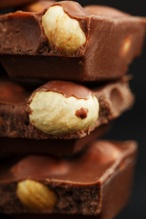 Chocolate with hazelnut in the form of a tower on a dark background. Pieces of milk chocolate with...