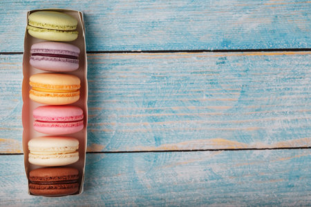 Macaroni cookies of different colors in a box on a blue, old wooden background of blue color. Free space. The concept of minimalismの写真素材