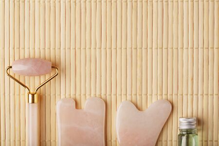 Gua sha massage made of natural rose Quartz-roller, jade stone and oil, on a bamboo background for face and body care. Copy the space for your text. Chinese medicine.の写真素材