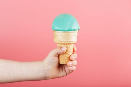 Ice cream in a child's hand melts on a pink background. The waffle cone with blue ice cream melts. Minimalistic concept, free space for text.の写真素材