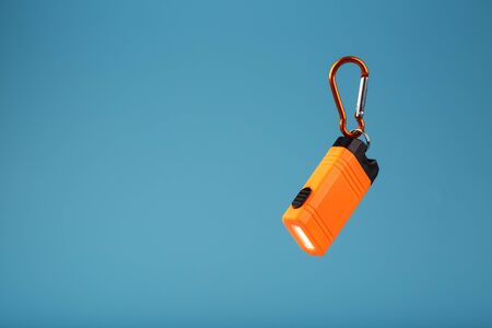 Orange led Flashlight with a carabiner on a blue background. LED lights in flight. Free space for text. Conceptの写真素材
