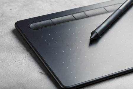 Graphic tablet with a stylus on a dark textural background, top view. Gadget for working as a...