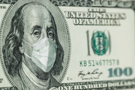 Portrait of Benjamin Franklin 100 dollar Bills with a medical mask from the coronavirus COVID-19. The COVID virus outbreak is affecting the global stock market and economy. The concept of the Financial crisis and pandemics.の写真素材