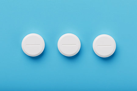 Round medicinal tablets lie in a row on a blue background, isolate. the view from the top, place for...