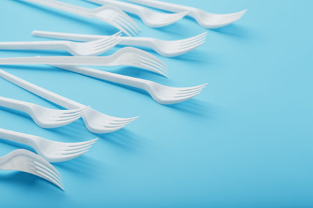 White plastic forks of disposable tableware on a blue background. Free space, top view.