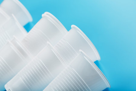 Plastic cups of disposable tableware on a blue background. Free space, top view.