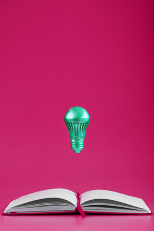 The light bulb hovers over the open pages of an empty notebook on a pink background. Minimalistic...