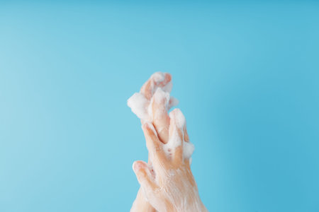 Children's hands in soap suds, on a blue background close-up, top view. Minimalistic concept of free...