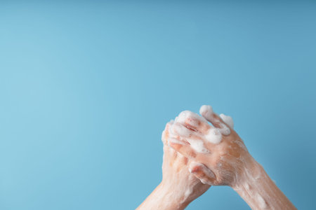 Children's hands in soap suds, on a blue background close-up, top view. Minimalistic concept of free...