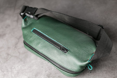 Belt bag made of dark green textured leather, banana on a gray background. Handmadeの写真素材