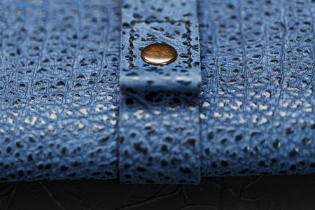 Blue purse made of textured leather on a black background. Handmade product close-up, macro....