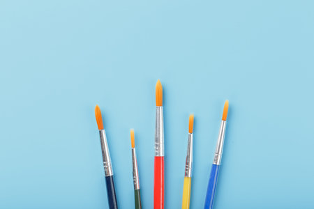 Brushes of different colors for drawing, creativity and art on a blue background. Top view, free...