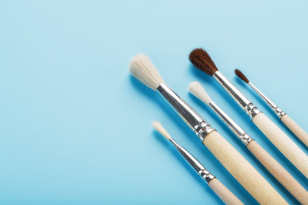 Brushes for drawing with paints made of natural wood and wool on a blue background. Free space