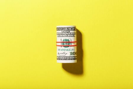 A roll of hundred-dollar American bills is tied with a red elastic band on a yellow background. Isolate. 100 dollars of currencyの写真素材