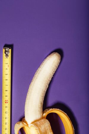 A banana is measured using a yellow ruler on a purple background. Concept of the male penis symbol. Adult materialの写真素材