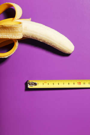 Yellow banana penis concept measured by measuring tape on pink background. Comparison of the size of a man's dignity. Free spaceの写真素材