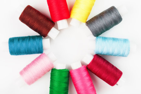 Sewing threads of different colors on reels on a white background in a circle.