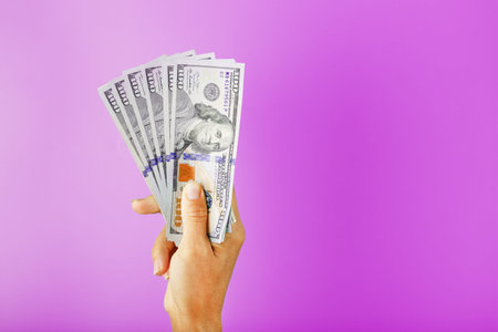 New dollar bills in hand on a pink background. The concept of financial assistance.