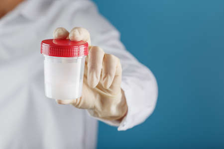 Semen analysis in a Bank is held in the hand of a doctor. Infertility. Doctors hand over a container for analysis. Health and conception. Free space on a blue background.の写真素材