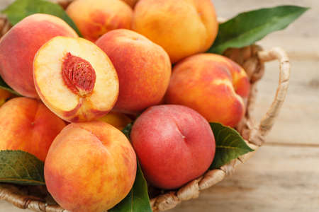 Peaches in a basket on a wooden background with a slice of sliced juicy peach with a stone. Rustic styleの写真素材