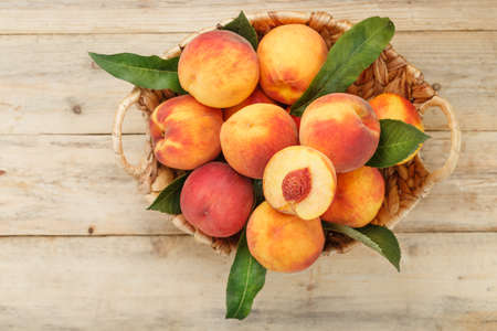Peaches in a basket on a wooden background with a slice of sliced juicy peach with a stone. Rustic styleの写真素材