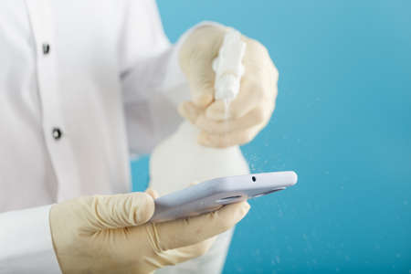 A man in Gloves handles the phone with a spray from a disinfectant. On a blue backgroundの写真素材