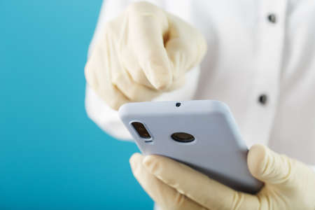 Smartphone in rubber gloves holding and using the touch screen of the smartphone, the concept of protection against the spread of viral infections. Close upの写真素材