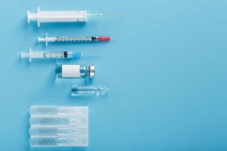 A set of medical syringes and ampoules with medicines and vaccines in a row on a blue background. Research of medicines for flu, measles, vaccine disease, pandemic. The view from the topの写真素材