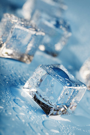 Close-up ice cubes with melt water drops scattered on a blue background. Macro. Refreshing ice for...