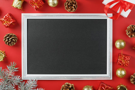 Photo frame with free black space around Christmas decorations and gifts on a red background. Top...