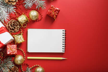 Christmas composition with notepad and a pencil for writing wishes with Christmas tree decorations on a red background. Christmas mood and plans for the future. View from above.の写真素材