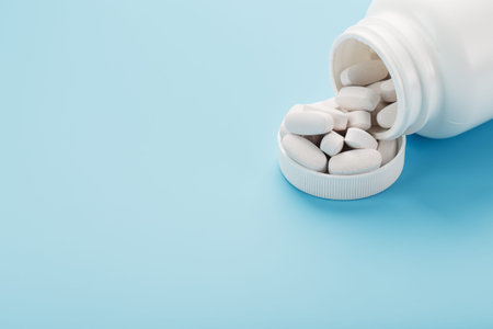 White capsules with vitamins and minerals in the form are poured from a jar on a blue background....