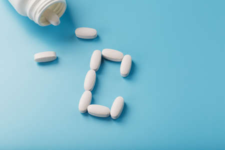 White capsules with vitamins in the form of C are poured from a jar on a blue background. Free spaceの写真素材