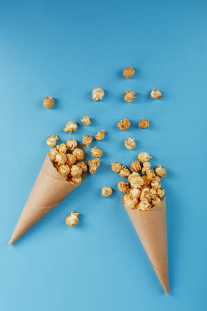 Caramel popcorn in a paper envelope on a blue background. Delicious praise for watching movie movies, serial, cartoon. Free space, close-up. Minimalistic concept.の写真素材