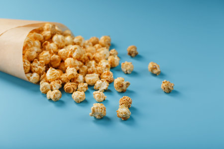 Popcorn in caramel glaze in a paper envelope on a blue background. Delicious praise for watching...