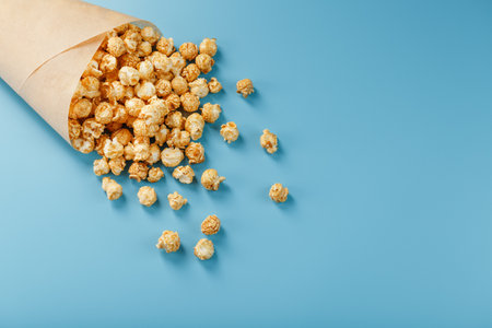 Popcorn in caramel glaze in a paper envelope on a blue background. Delicious praise for watching movie movies, serial, cartoon. Free space, top view. Minimalistic concept.の写真素材