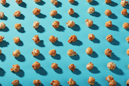 Patterns of caramel popcorn on a blue background in the form of a pattern. Full screen as a conceptual background. Hard light with shadowの写真素材