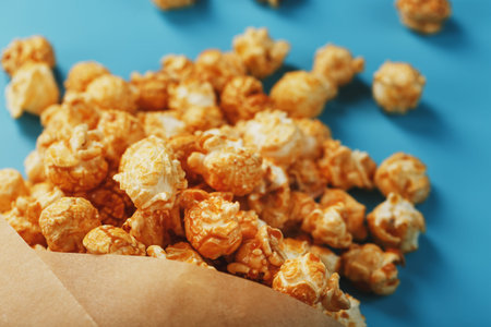 Caramel popcorn in a paper envelope on a blue background. Delicious praise for watching movie...