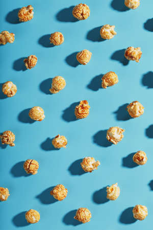 Patterns of caramel popcorn on a blue background in the form of a pattern. Full screen as a conceptual background. Hard light with shadowの写真素材