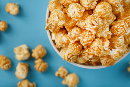 Caramel of the popcorn in a white cup with a scissor on a blue background. Delicious catch for the films of movies, serials, cartoons. Free rightful, crimes. Minimalistic concession.の写真素材