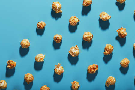 Patterns of caramel popcorn on a blue background in the form of a pattern. Full screen as a conceptual background. Hard light with shadowの写真素材